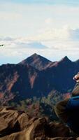 Vertical Male influencer shares his hiking journey through a vlog with the drone, recording high quality aerial view content with remote control. Young hiker content creator filming the scenery. Camera A. video