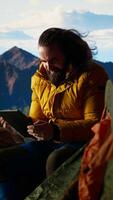 Vertical Male hiker struggles to work online in windy conditions on a remote mountain peak. Battling weak signals and cold weather, explorer is obsessed with technology and the internet. Camera A. video