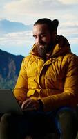 vertical jovem explorador mantém trabalhando às a topo do a montanha com Internet em todos os lugares, desfrutando global conectividade e produtividade em a Colina cume. Alto Rapidez Forte sinal em uma caminhada. Câmera uma. video