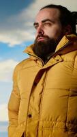 Vertical Nature lover stands at the edge of a breathtaking mountain range, looking at the scenic background of towering peaks and vast sky. Young man enjoying adventure and outdoor exploration. Camera B. video