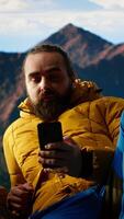 Vertical Traveler in warm clothing scrolling social media on top of the mountain peak, person always connected with a strong signal and obsessed with technology. Climbing the hills. Camera B. video