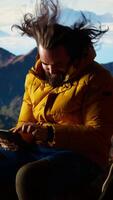 Vertical Traveler tries to stay connected in the wilderness but struggles with weak signals, dangerous wind at the top of the mountain. Hiker setting up his tent on a rocky windy peak. Camera A. video