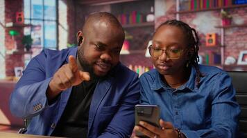 African american man and woman sit at the desk discussing freelance strategies, researching marketing trends on phone to create a helpful report. Couple doing teamwork. Camera A. video