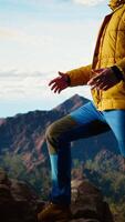 Vertical Proud explorer basks in the joy of accomplishment standing at the mountain peak with arms lifted, mindfulness. Traveler admiring stunning scenic view and vast sky for the thrill of hiking. Camera A. video