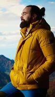 Vertical Hiker dressed in warm clothing stands on a mountain peak after climbing to the top, gazing at the breathtaking landscape of rugged hills and vast sky. Adventure with scenic view. Camera A. video
