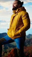 Vertical Adventure seeker in warm clothing enjoys the serenity of the wilderness, panoramic mountain top view and open sky create the perfect setting for relaxation. Cold winds uphill. Camera A. video