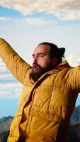 Vertical Satisfied adventure seeker stands at the top a towering mountain, taking in the epic view and feeling proud of his hiking achievement. Strong joyful trekker feels the rewarding experience. Camera B. video