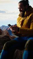 Vertical Trekker enjoys a quiet moment in the mountains scrolling phone app, where the high altitude air and breathtaking view encourage mindfulness. Relaxation and self improvement. Camera A. video