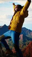Vertical Satisfied adventure seeker stands at the top a towering mountain, taking in the epic view and feeling proud of his hiking achievement. Strong joyful trekker feels the rewarding experience. Camera A. video