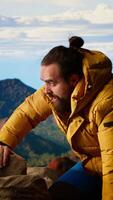 Vertical Proud explorer celebrates on top of a high altitude mountain peak, surrounded by rugged hills and dramatic clouds. Triumphant pose captures the thrill of climbing to success. Camera B. video