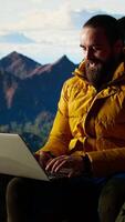 Vertical Tech savvy hiker having a technology obsession and working on a mountain peak, always connected to the internet with strong signal. Workaholic traveler does remote work on a hill. Camera A. video