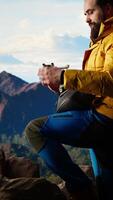 Vertical Modern traveler creating content and filming the valley with his drone, climbing on top of a high altitude mountain range. Hiker enjoying the landscape scenery, remote control. Camera A. video