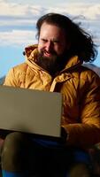 Vertical Hiker defies the harsh winds and cold weather to stay connected online, camping in the windy risky wilderness. Explorer with technology addiction connected even on mountain top. Camera B. video