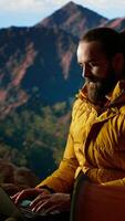 vertical jovem explorador mantém trabalhando às a topo do a montanha com Internet em todos os lugares, desfrutando global conectividade e produtividade em a Colina cume. Alto Rapidez Forte sinal em uma caminhada. Câmera b. video