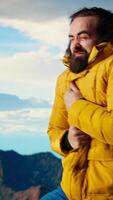 Vertical Young traveler hiker dealing with cold weather and wind at the mountain top, feeling proud with his personal achievement. Nature lover struggles to climb due to bad weather. Camera A. video