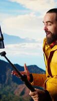 Vertical Vlogger recording a with a smartphone on a tripod capturing a panoramic view of the mountains from a rocky peak. Content creator shares his passion for travel and nature. Camera A. video