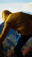Vertical Young adventure seeker taking photos on the mountain top using his phone, capturing the moment of his achievement. Nature lover hiker climbing the mountain range and sitting on the peak. Camera A. video