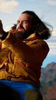 Vertical Reckless explorer struggling with wind and weak signal keep internet connection, camping on a scenic rocky mountain peak. Hiker in danger with extreme cold weather, foolish. Camera B. video