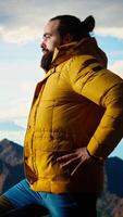 Vertical Nature lover stands at the edge of a breathtaking mountain range, looking at the scenic background of towering peaks and vast sky. Young man enjoying adventure and outdoor exploration. Camera A. video