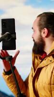 Vertical Traveler filming his hiking experience in the wilderness documenting his adventure on social media using his smartphone. Recording the beautiful scenic mountain view behind him for content. Camera B. video
