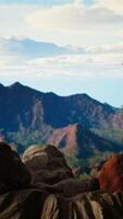 Vertical Battling intense wind and searching for better telephone signal, young hiker acting reckless distracted by smartphone on mountain top. Tumbling on the steep cliffs of a scenic peak. Camera A. video