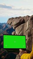 Vertical Young traveler embraces high altitude wilderness next to chroma key, using a device where the crisp air and scenic mountain view provide an inspiring setting for adventure. Camera A. video