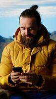 Vertical Nature lover relaxing on mountain top getting online with his phone at a scenic viewpoint, looking out over the landscape. Hiker staying always online and connected, panoramic scenery. Camera B. video