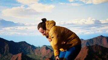 Reckless unprepared hiker stumbles near the edge of a high altitude cliff, caught off guard by strong winds. Unequipped for the extreme conditions, losing balance on mountain top. Camera B. video