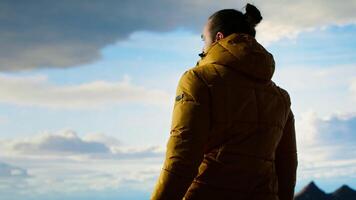 Traveler stands alone at the edge of a towering mountain range, gazing at the clouds and stunning panoramic scenery. Man showcasing personal growth and perseverance. Camera B. video