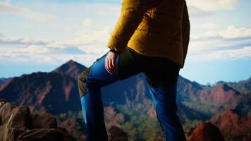 Traveler stands alone at the edge of a towering mountain range, gazing at the clouds and stunning panoramic scenery. Man showcasing personal growth and perseverance. Camera A. video
