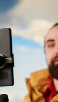 Vertical Vlogger recording a with a smartphone on a tripod capturing a panoramic view of the mountains from a rocky peak. Content creator shares his passion for travel and nature. Camera B. video