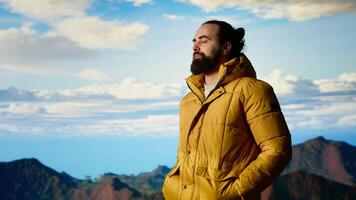 Hiker dressed in warm clothing stands on a mountain peak after climbing to the top, gazing at the breathtaking landscape of rugged hills and vast sky. Adventure with scenic view. Camera B. video