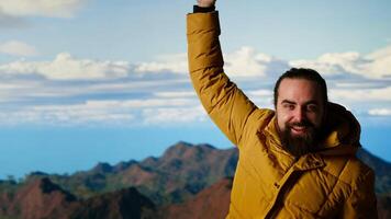 Triumphant hiker stands at the mountain peak with his arms raised in victory, celebrating success and personal achievement of climbing another mountain. Breathtaking panoramic view. Camera B. video