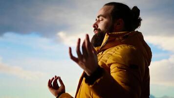 Adventure seeker doing a meditation pose on top of the mountain, successfully climbing the hill and enjoying the scenic landscape. Young calm zen traveler hiking and meditating. Camera B. video