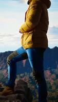 Vertical Hiker gazes at the panoramic view of dramatic mountain peaks and clouds, feeling the thrill of adventure and rewards of perseverance. The journey represents strength and personal growth. Camera A. video