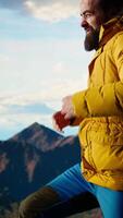 Vertikale jung Reisender kämpfen mit kalt Winde auf oben von das Berg, Gefühl stolz von seine Trekking Aktivität. Abenteuer Sucher mit Ambition erfolgreich Klettern das Berg Bereich. Kamera a. video