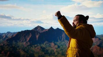 Hiker reaches the top of a mountain and does a victorious pose after a successful climb, reflecting confidence for adventure. Traveler enjoying the personal achievement of conquering fears. Camera A. video