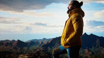 Explorer stands on a mountain peak taking in the fresh air and panoramic scenery. Hiker admires the stunning landscape of rugged peaks and vast sky, adventure and sightseeing. Camera B. video