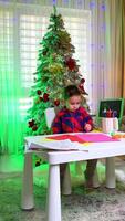 Child working on crafts in festive room. A young child is creating colorful artwork at a white table, surrounded by a beautifully decorated Christmas tree. video