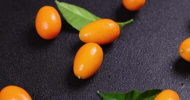 Fresh kumquats falling and bouncing on a black surface, creating a visually appealing display with green leaves video