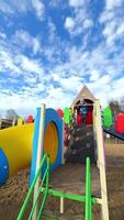 Kids play at a bright, fun park. A child climbs on a vibrant playground slide under a sunny sky filled with fluffy clouds, enjoying outdoor playtime. video