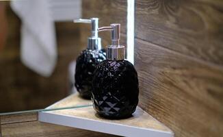The bottle of a soap dispenser and is placed on a shelf next to a mirror photo