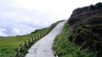 A path winds up a hillside with a fence on the side photo