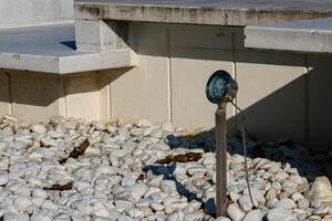 Ground-level garden light illuminates a pebble pathway in daylight photo