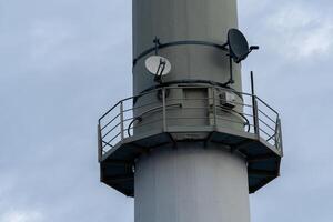 Satellite dish mounted on tall communication tower against cloudy sky photo