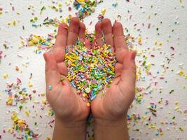 Close-up of child's hands playing with colorful sprinkles on table. Heart-shaped sprinkles in a child's hands. photo