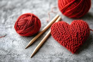 A knitted red heart with knitting needles and a ball of red thread lies on a concrete surface. Knitting. Valentine's Day. A DIY photo