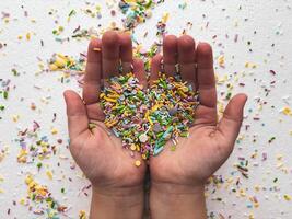 Close-up of child's hands playing with colorful sprinkles on table. Heart-shaped sprinkles in a child's hands photo