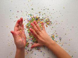 Child playing with colored sugar candies on white background. Confectionery sprinkles in child's palms. Children's game, fine motor skills photo
