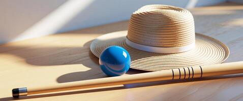 A straw hat a pool ball and a pool cue arranged on a wooden surface. photo
